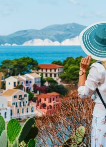 tourist-female-with-blue-sun-hat-and-travel-backpack-enjoying-greek-vivid-colored-assos-town-768x512