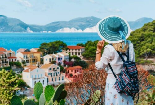 tourist-female-with-blue-sun-hat-and-travel-backpack-enjoying-greek-vivid-colored-assos-town-768x512