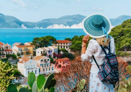 tourist-female-with-blue-sun-hat-and-travel-backpack-enjoying-greek-vivid-colored-assos-town-768x512